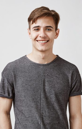 young-man-with-charming-smile-blue-eyes-posing Handsome boyfriend smiles and looks to the camera. Young man is very glad his girlfriend got a promotion. He can not celebrate with her today, but they will arrange something on weekend. Copy space